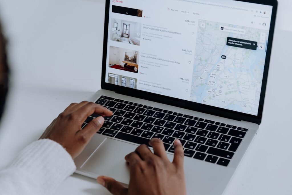 pexels-photo-5077049-1 Hands typing on laptop searching Airbnb for accommodation options with map view.